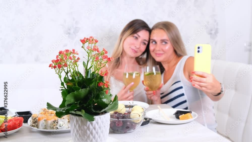 friendship and party concept - two young beautiful girlfriends drink wine and take selfie on smartphone in a cozy kitchen at the table, selective focus friendship and party concept - two young beautiful girlfriends drink wine and take selfie on smartphone in a cozy kitchen at the table, selective focus