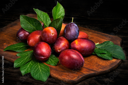 Ripe juicy plums with leaves on a cutting board wooden background.