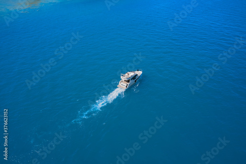 Lonely boat, movement on the water. Aerial view of a white yacht near the shore on blue water. luxury motor boat. Top view of a white boat sailing in the blue sea. Drone view of a boat.