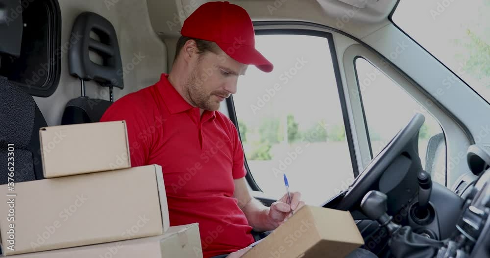 delivery service man sitting in van and writing documents on clipboard before delivering a package to customer delivery service man sitting in van and writing documents on clipboard before delivering a package to customer