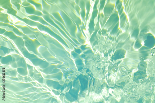 Closeup of mint green transparent clear calm water surface texture with splashes and bubbles. Trendy abstract summer nature background. Mint colored waves in sunlight. 