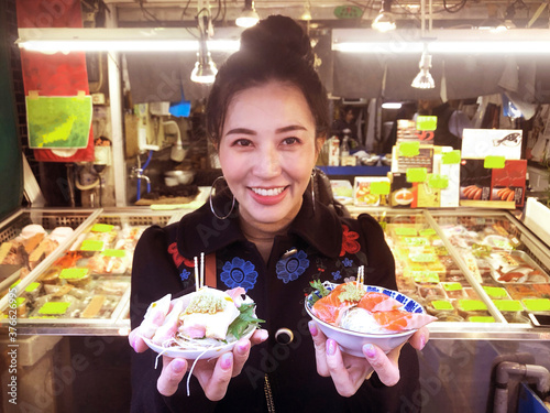 Tourist woman showing salmon sashimi most popular delicious food in street food tsukiji fish market, Japan