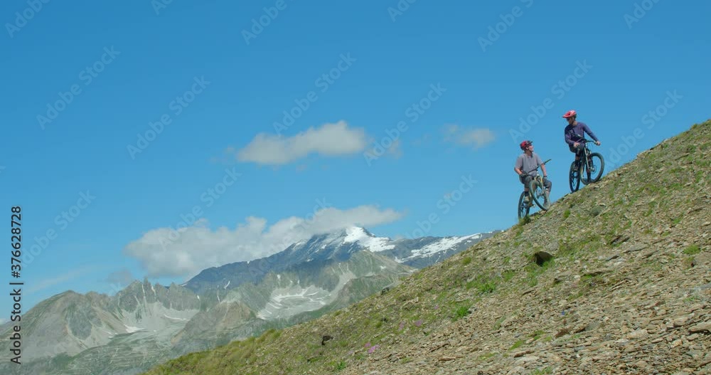 Two mountain bikers on a mountainside with glaciers in background discuss their options and route. Two mountain bikers on a mountainside with glaciers in background discuss their options and route.