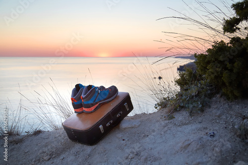 Passion for travel. Summer holiday. Adventure time. Boots and suitcase on sand. Lovely sunset. Virgin nature. Blue sky