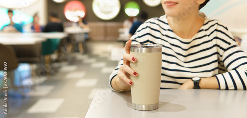 Fotografie Hand of stylish Asian woman holding beautiful reusable insulated tumbler and smiling in modern restaurant / food court