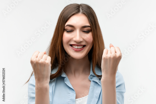 Image of young happy woman smiling and making winner gesture. Studio shot, white background, isolated