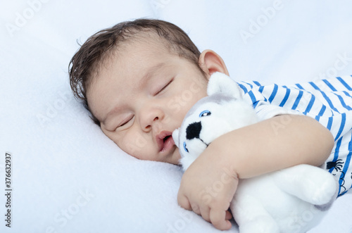 Retrato de primer plano de bebé recién nacido durmiendo, abrazando perro de peluche.