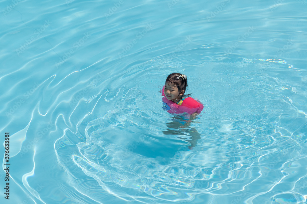 Asian cute little toddler girl in a colorful swimming suit relaxing in a pool.