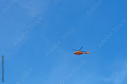 A small helicopter is flying high in the blue sky