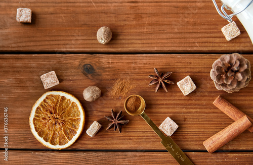 christmas and seasonal drinks concept - aromatic spices, brown sugar, nutmeg and pine cone on wooden background