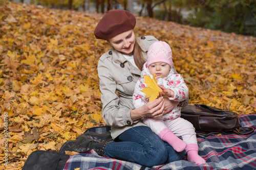 Young beautiful mother and child in autumn Park on yellow foliage background photo