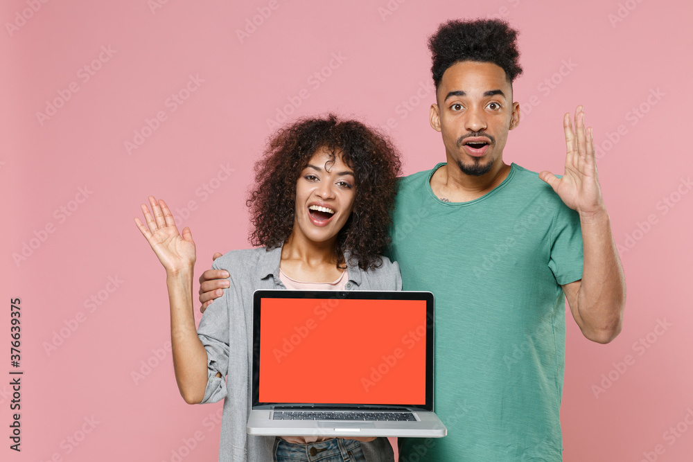 Excited african american couple friends guy girl in gray green clothes hold laptop computer with blank empty screen mock up copy space spreading hands isolated on pink wall background studio portrait. Excited african american couple friends guy girl in gray green clothes hold laptop computer with blank empty screen mock up copy space spreading hands isolated on pink wall background studio portrait.
