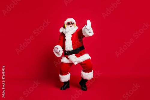 Full body size photo of pensioner old man grey beard chilling middle dance floor wear santa costume gloves coat belt sunglass headwear earphones black boots isolated red color background