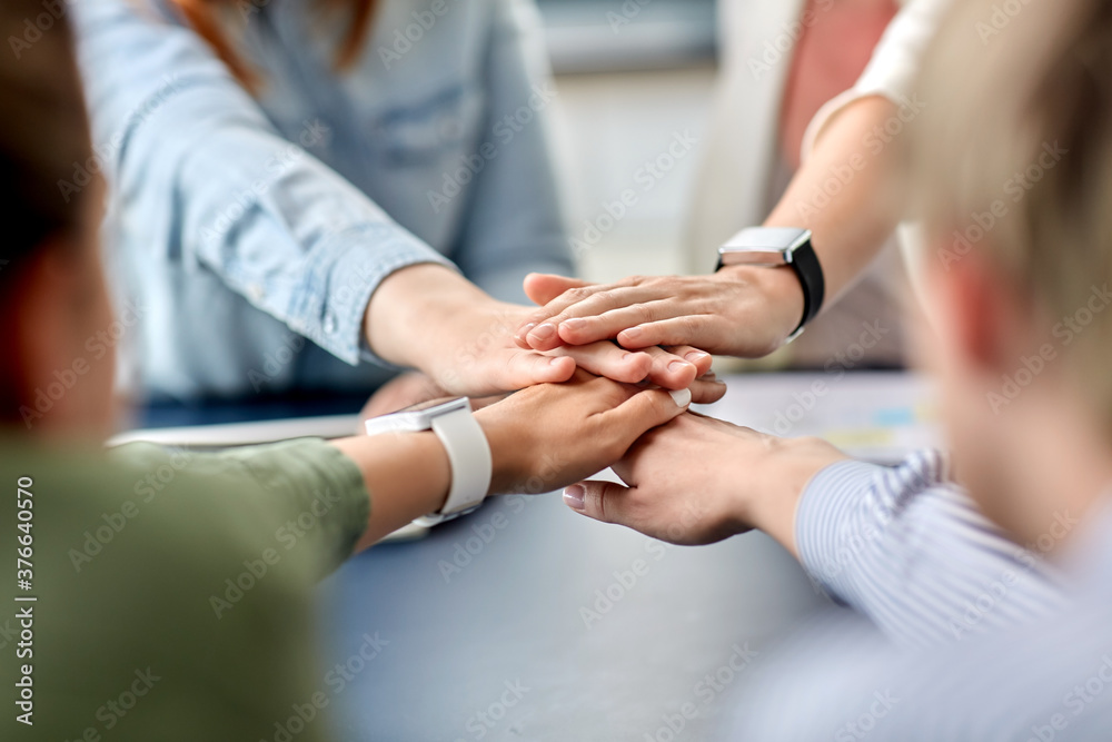Fototapeta premium cooperation, corporate and team work concept - close up of business team stacking hands at office