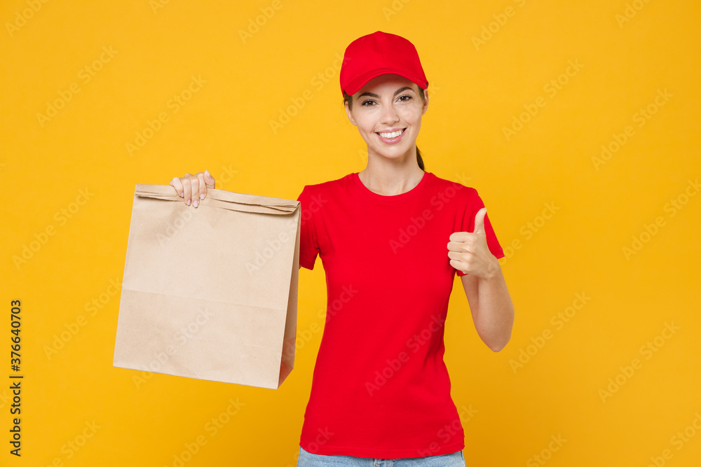 Delivery employee woman in red cap blank t-shirt uniform work courier service from shop restaurant to home office hold in hand brown craft paper takeaway food bag mockup isolated on yellow background. Delivery employee woman in red cap blank t-shirt uniform work courier service from shop restaurant to home office hold in hand brown craft paper takeaway food bag mockup isolated on yellow background.