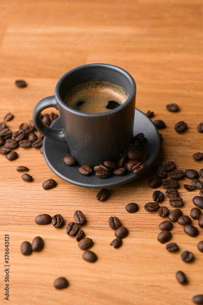 A grey cup of coffee on a wooden table with fresh coffee beans around with against a dark background A grey cup of coffee on a wooden table with fresh coffee beans around with against a dark background