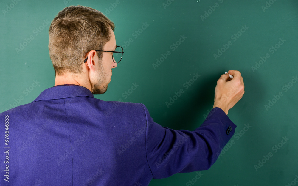 Teacher write on chalkboard rear view, explaining to students concept Teacher write on chalkboard rear view, explaining to students concept