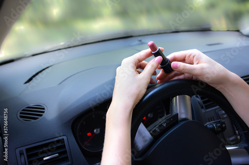 Woman is applying makeup in the car. Girl with lipstick behind the wheel. Dangerous driving situation on the road. Possibility of accident.