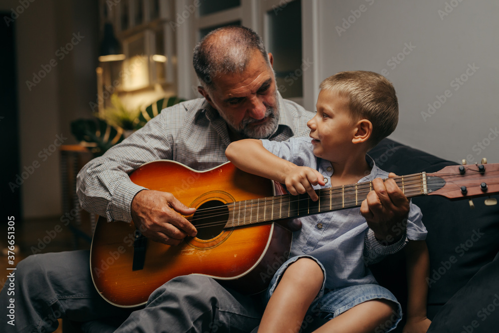 Obraz premium grandfather and his grandson relaxing on sofa at home playing guitar