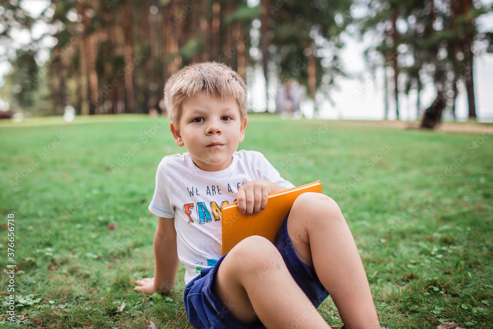Back to school. Kindergarten scholar sitting on green grass with book at open-air class Back to school. Kindergarten scholar sitting on green grass with book at open-air class