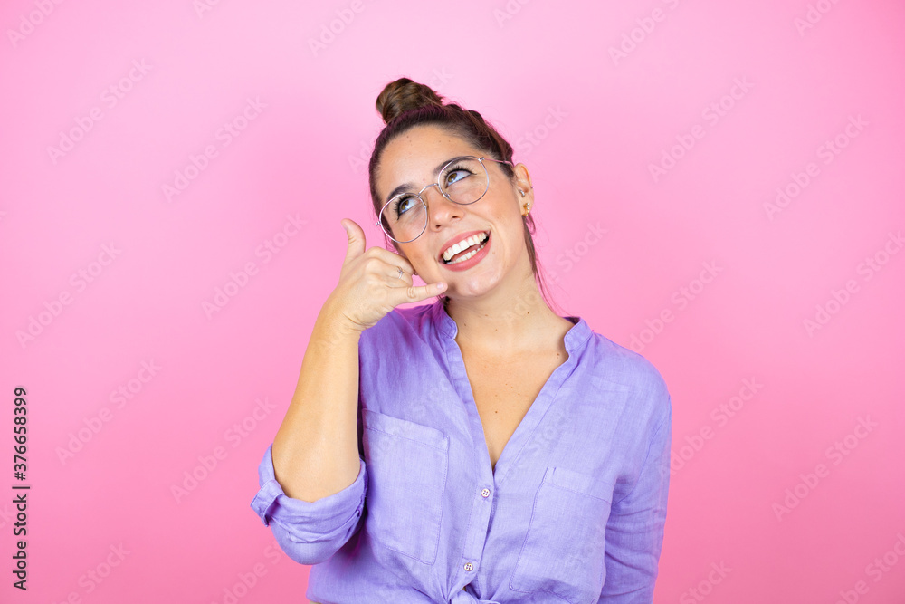 Young beautiful woman wearing glasses over isolated pink background smiling doing phone gesture with hand and fingers like talking on the telephone Young beautiful woman wearing glasses over isolated pink background smiling doing phone gesture with hand and fingers like talking on the telephone