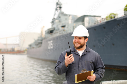 Marine first mate talking by walkie talkie and standing near vessel with documents.