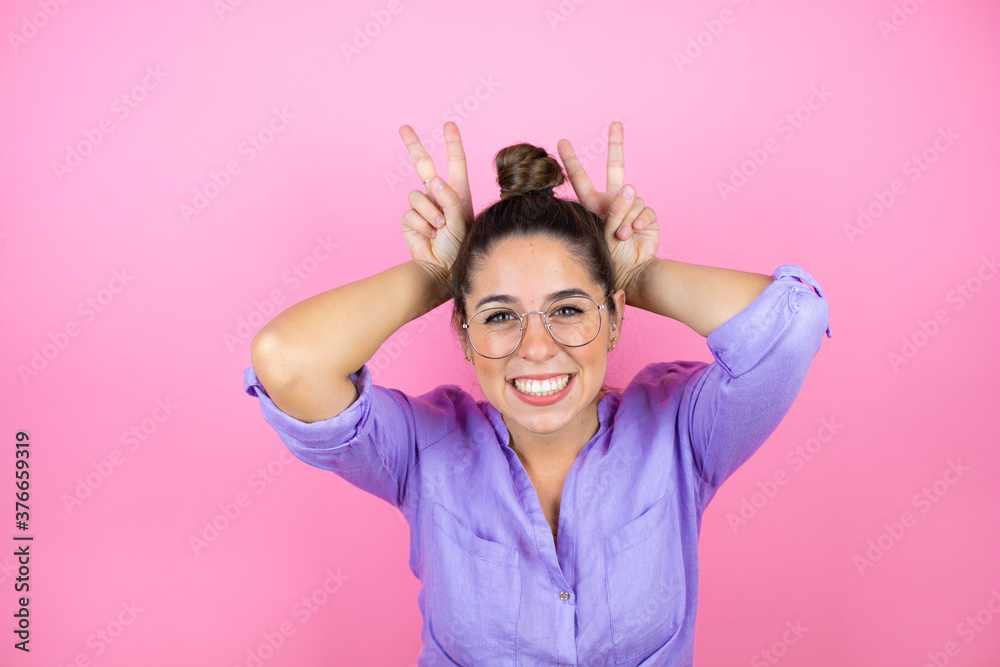 Young beautiful woman wearing glasses over isolated pink background Posing funny and crazy with fingers on head as bunny ears, smiling cheerful Young beautiful woman wearing glasses over isolated pink background Posing funny and crazy with fingers on head as bunny ears, smiling cheerful