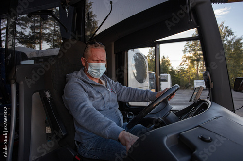 Bus driver wearing a medical mask, looking out of the bus window Safe driving during a pandemic, protection against coronavirus