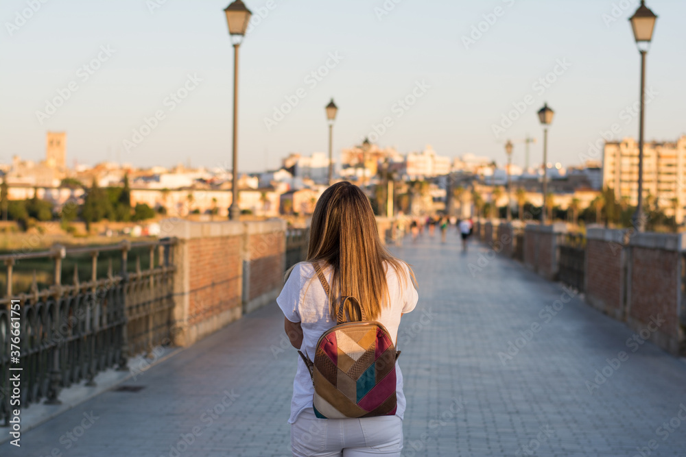 Fototapeta premium Rear view of a woman walking through the city using her mobile phone.