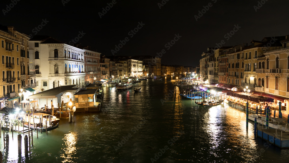 Nightly scene overlooking a canal with boat traffic in Venice. Some restaurants are waiting for customers.