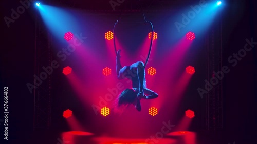 Air gymnastics woman performs acrobatics tricks on aerial hoop. Female doing some acrobatic elements on aerial hoop indoors. Silhouette. Slow motion.