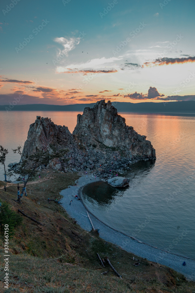 Cape Shamanka rock in clear blue Lake Baikal among rocks, coast, against the background of colorful sunset sky, evening clouds