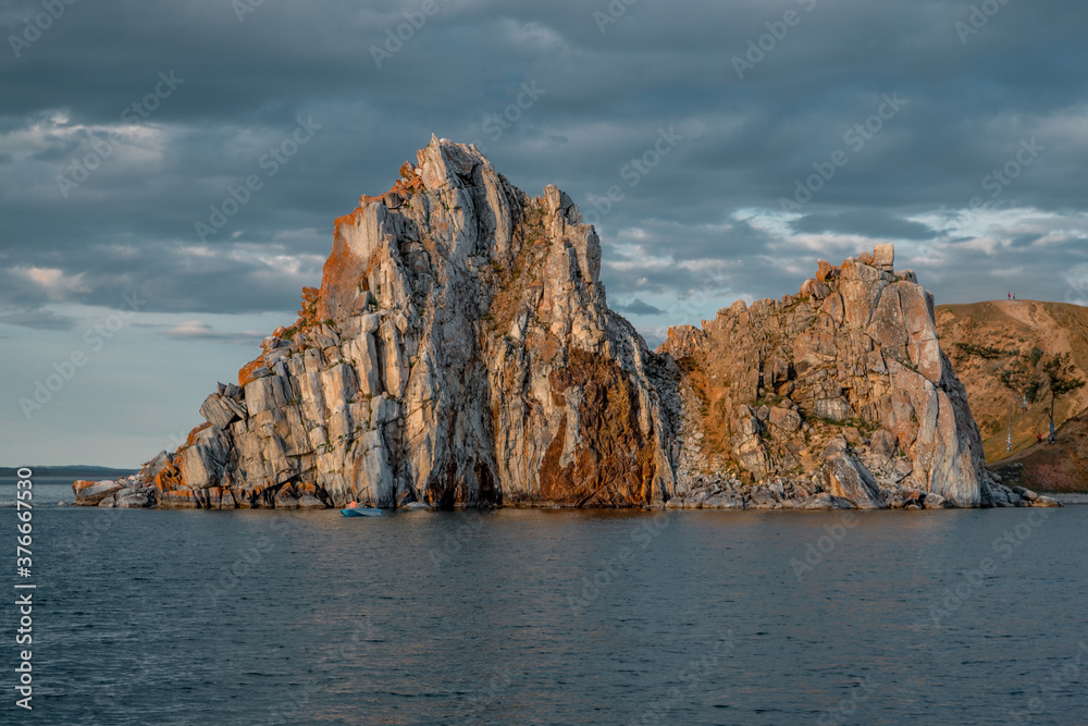 Cape Shamanka rock in blue Lake Baikal, background clouds, sunset light