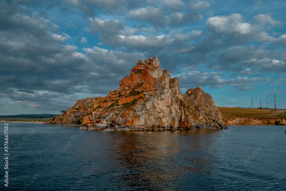 Red cape Shamanka rock in blue Lake Baikal, background clouds, sunset