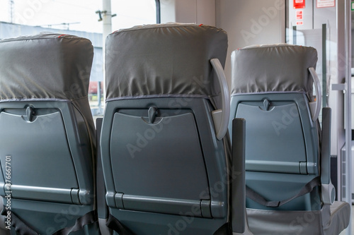Back view on passenger railroad train seats. Empty grey interior of urban express. New plastic seat cover in gray. City public transportation inside. Row of comfortable tourist armchairs with armrests