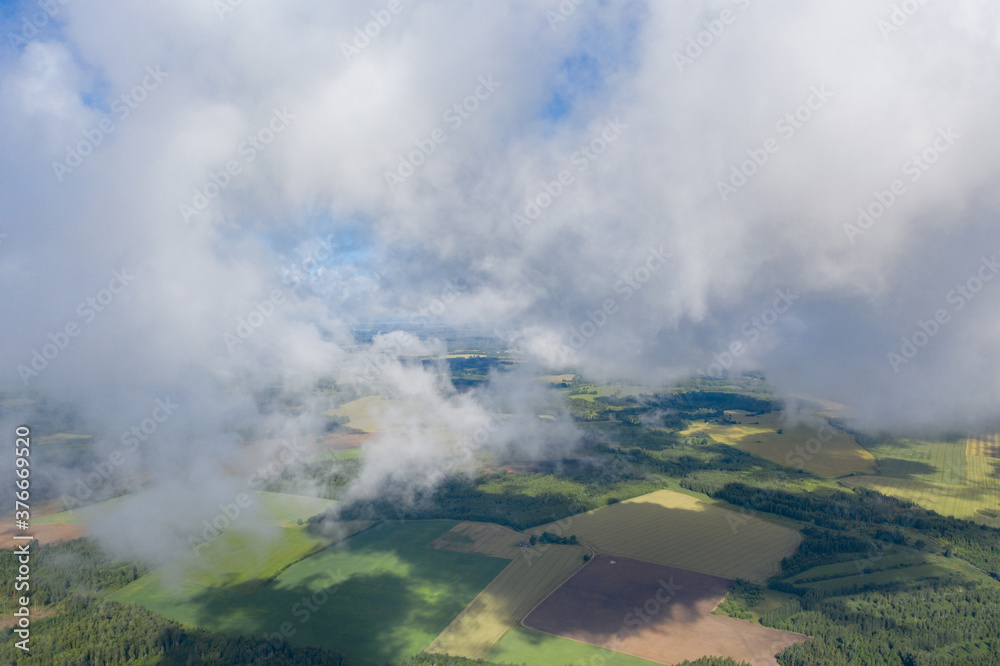 Aerial view of green farmland fields through white clouds
