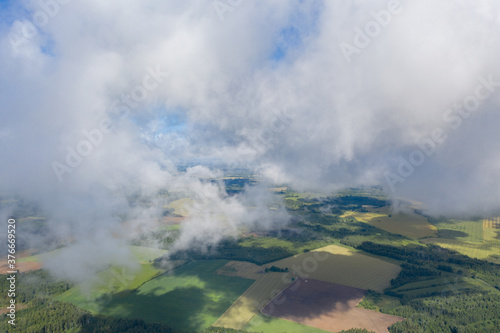 Aerial view of green farmland fields through white clouds © Abinieks