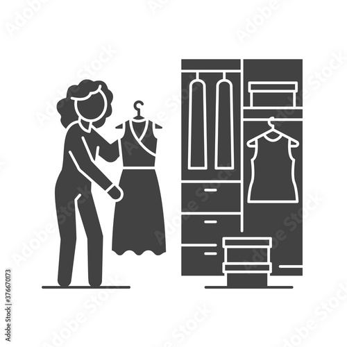 Woman standing in front of opened wardrobe with apparel hanging inside black glyph icon. Home leisure. Vector isolated illustration.