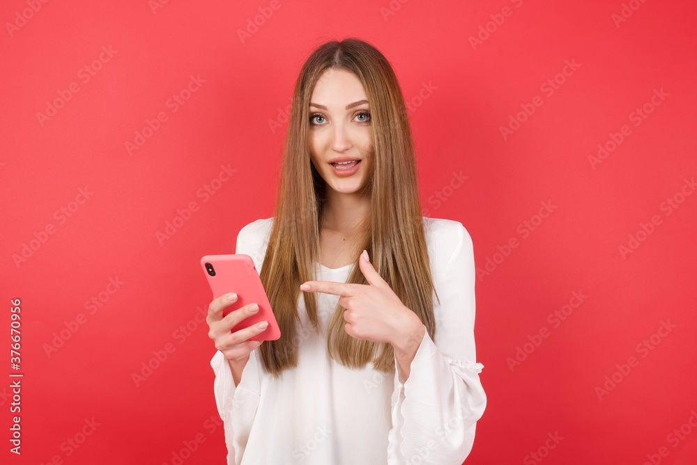 Eastern European woman holding bucket with popcorn standing over isolated red background holding in hands showing new cell, Eastern European woman holding bucket with popcorn standing over isolated red background holding in hands showing new cell,