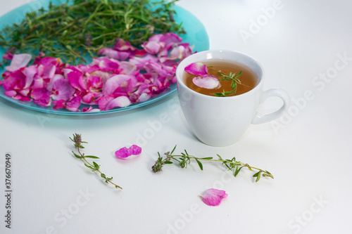 Homemade herbal tea in a white cup. Tea rose petals and thyme on a plate -ingredients for hot healthy drink