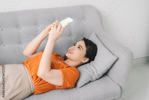 Attractive woman smiling as she reads an sms message on her mobile while relaxing on a sofa photo