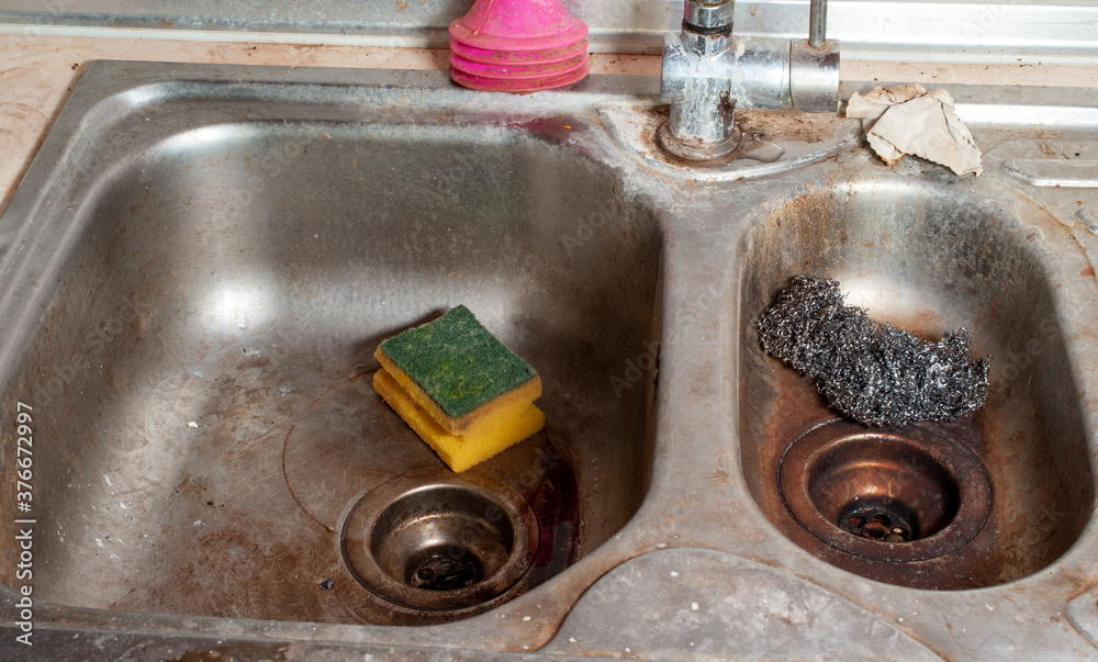 Steel dishwashing wool and dish sponge in a dirty metal sink