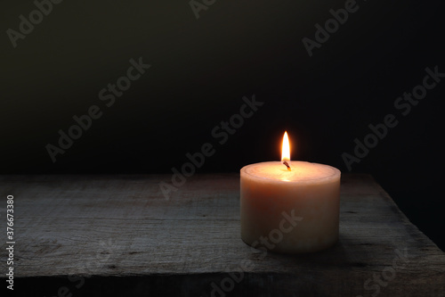 aroma scented ivory colour pillar candle lighting on the wooden table in the dark living room at night in the winter