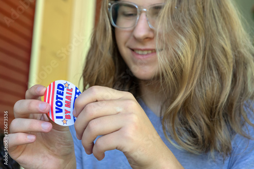 Young First time voter male peeling I voted by mail sticker, focus on sticker photo