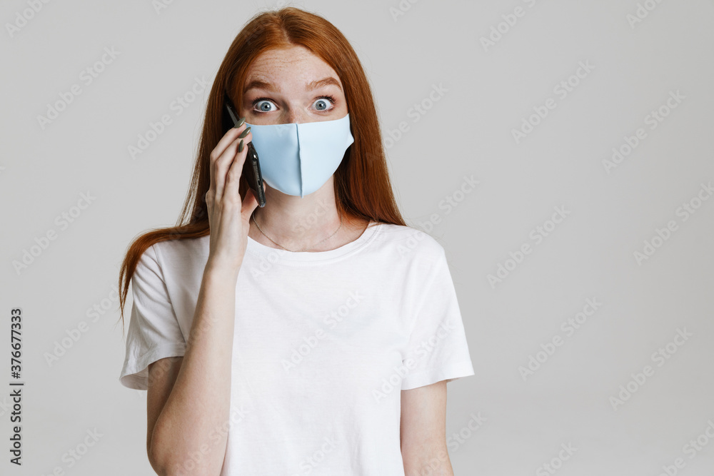 Image of surprised ginger girl in face mask talking on mobile phone Image of surprised ginger girl in face mask talking on mobile phone