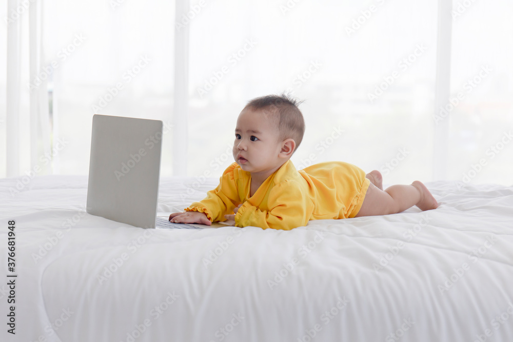 An Asian baby is playing on a laptop on a clean white bed. An Asian baby is playing on a laptop on a clean white bed.