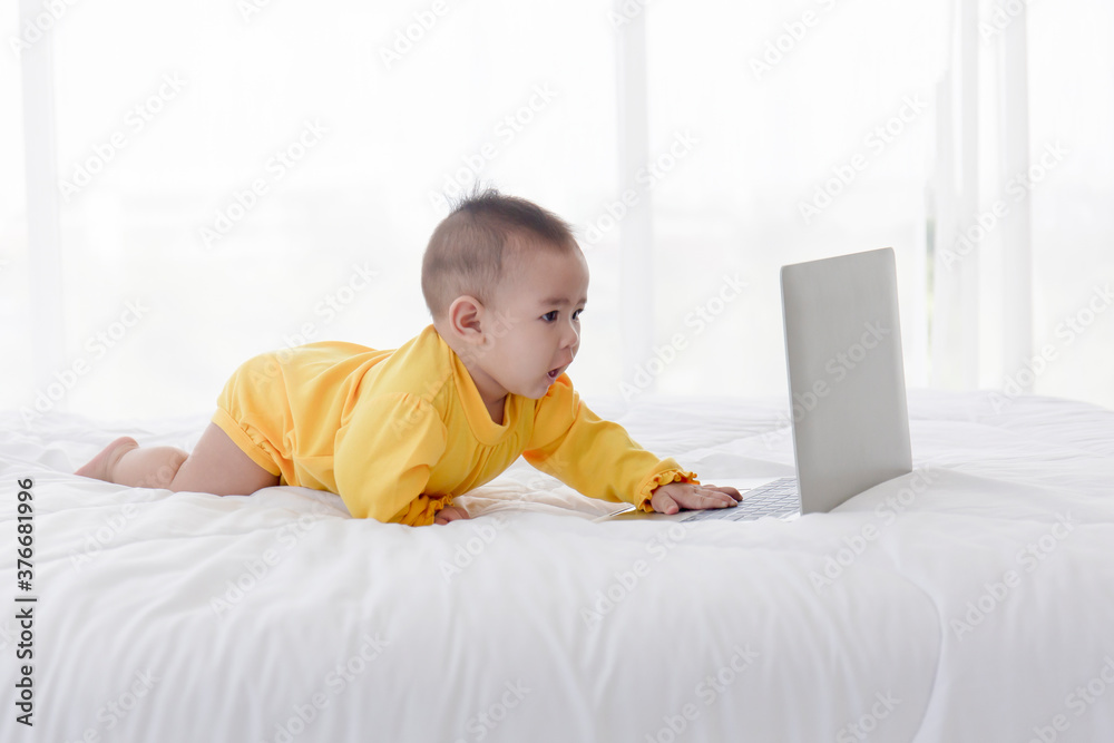 An Asian baby is playing on a laptop on a clean white bed. An Asian baby is playing on a laptop on a clean white bed.