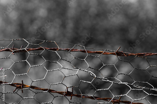 Rusted barbed wire through flimsy mesh wire fence. 