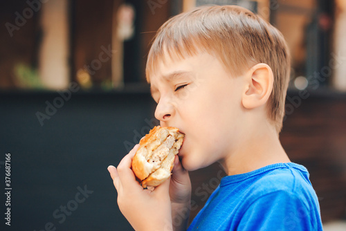 Hungry kid eating a burger at outdoors cafe.