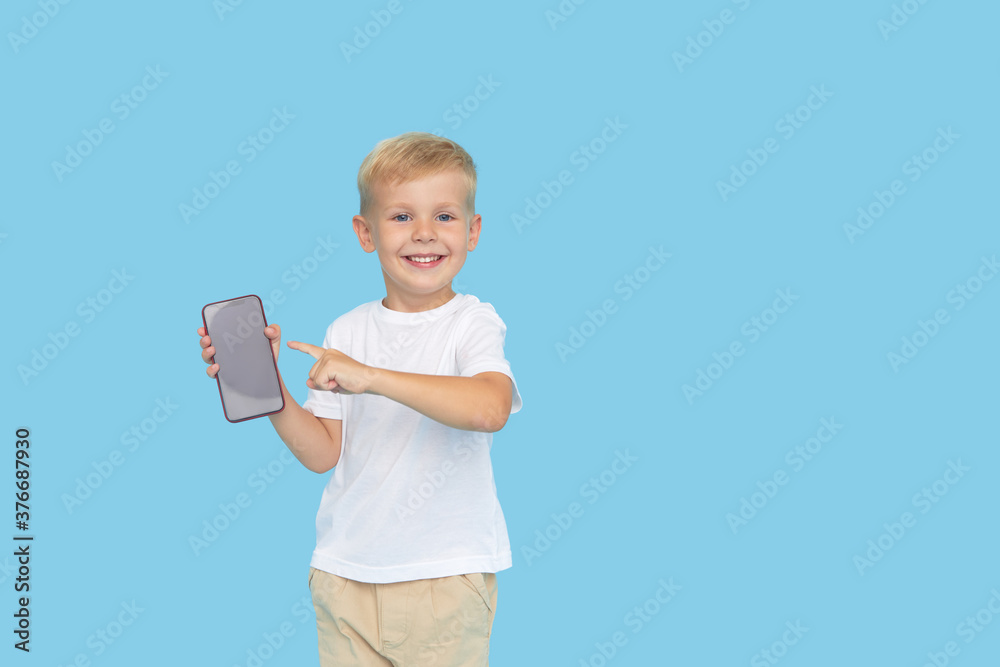 Cute smilling child boy with smartphone on blue background. Advertising of educational applications on a mobile phone for children. Funny face. Cute smilling child boy with smartphone on blue background. Advertising of educational applications on a mobile phone for children. Funny face.